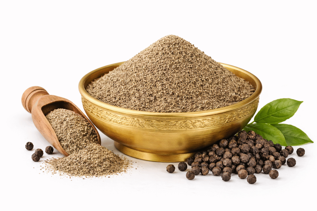 black pepper powder in brass bowl with whole peppercorns and wooden scoop